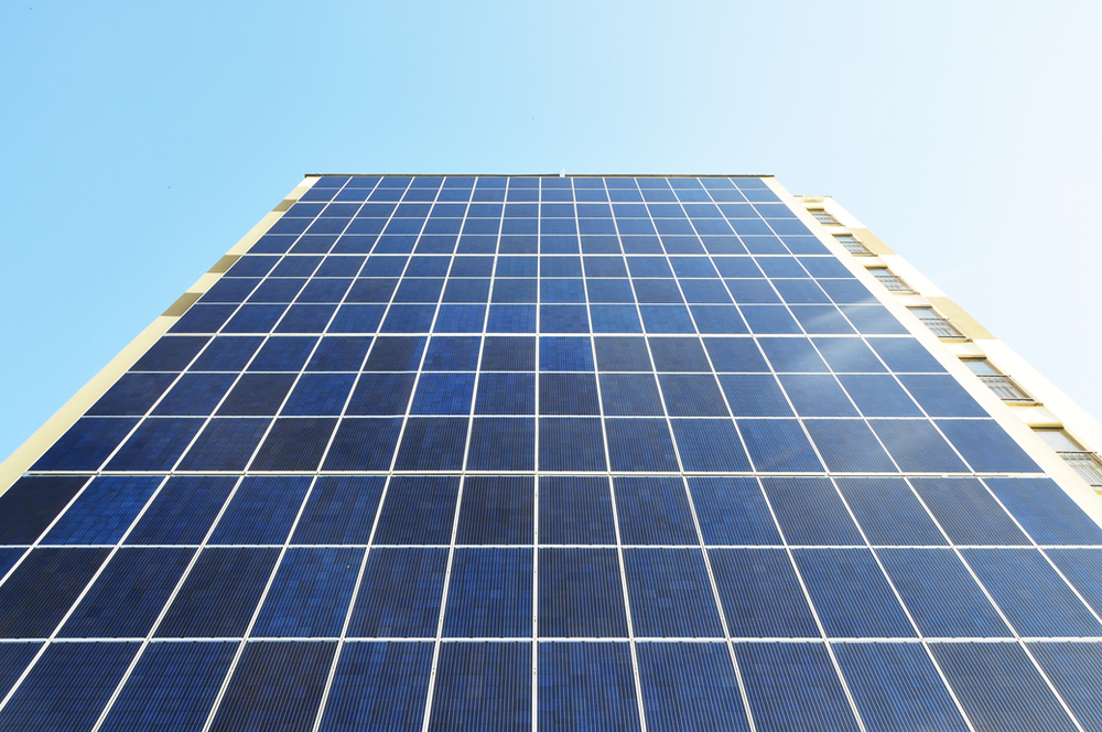 Looking up at a wall of dark blue solar cells integrated into the side of a tall building