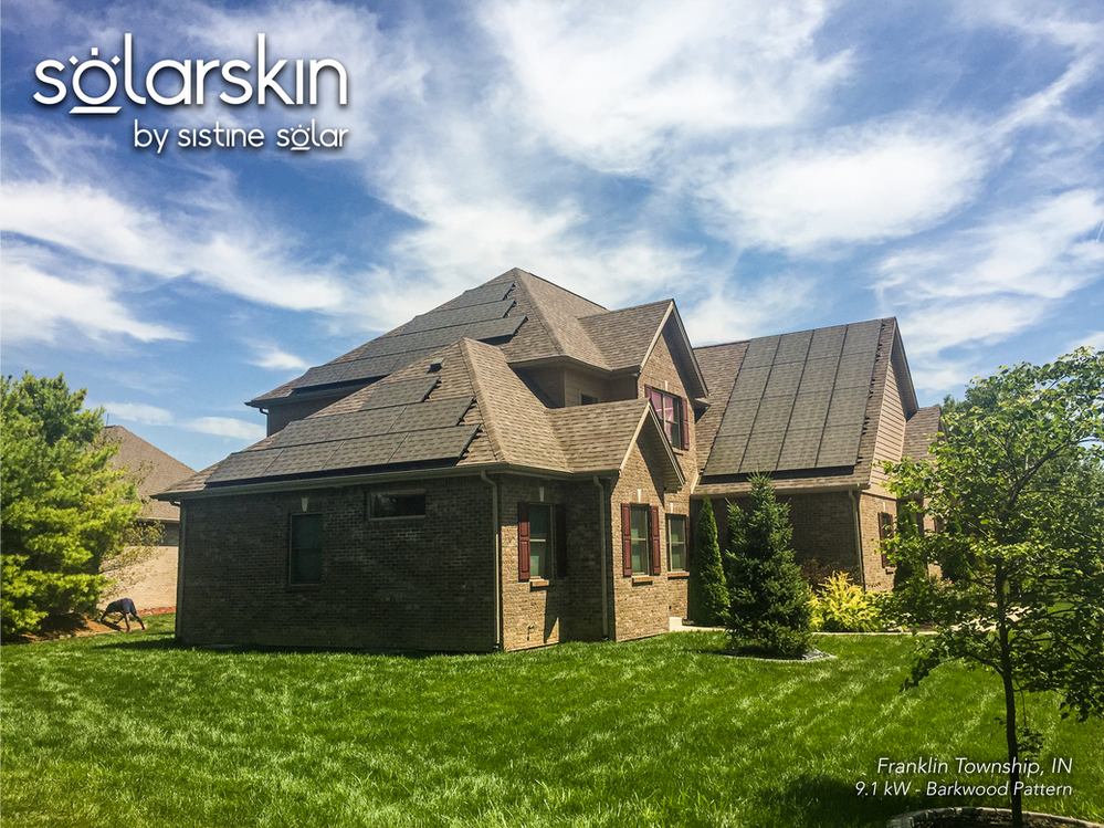 Single-family brown brick home under a clear sky, several solar arrays covered in matching brown tile SolarSkin on the roof facing street-side