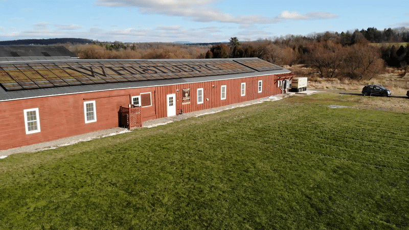 Panning over one side of long red distillery roof, featuring solar panels with barrel print design and WhiskeyPig logo on top